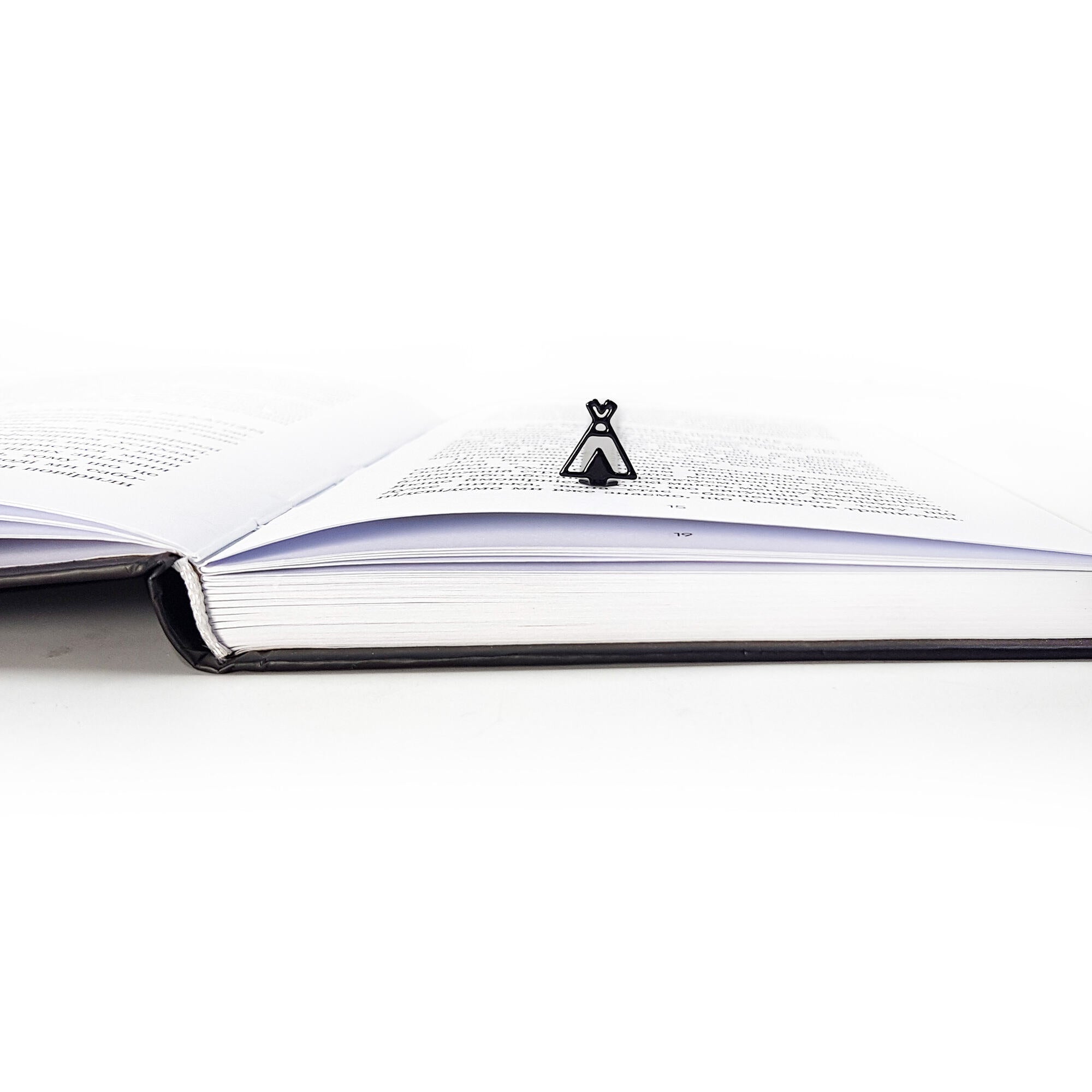 Side view of an open book with a black teepee-shaped metal bookmark standing upright between the pages.