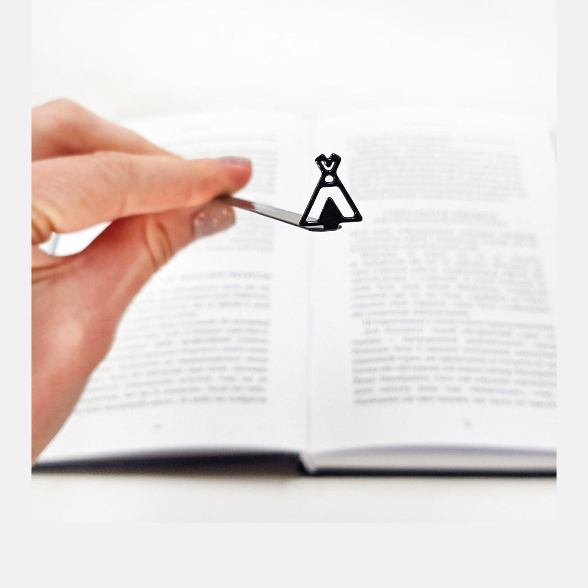 Teepee Tent metal bookmark held in a hand above an open book