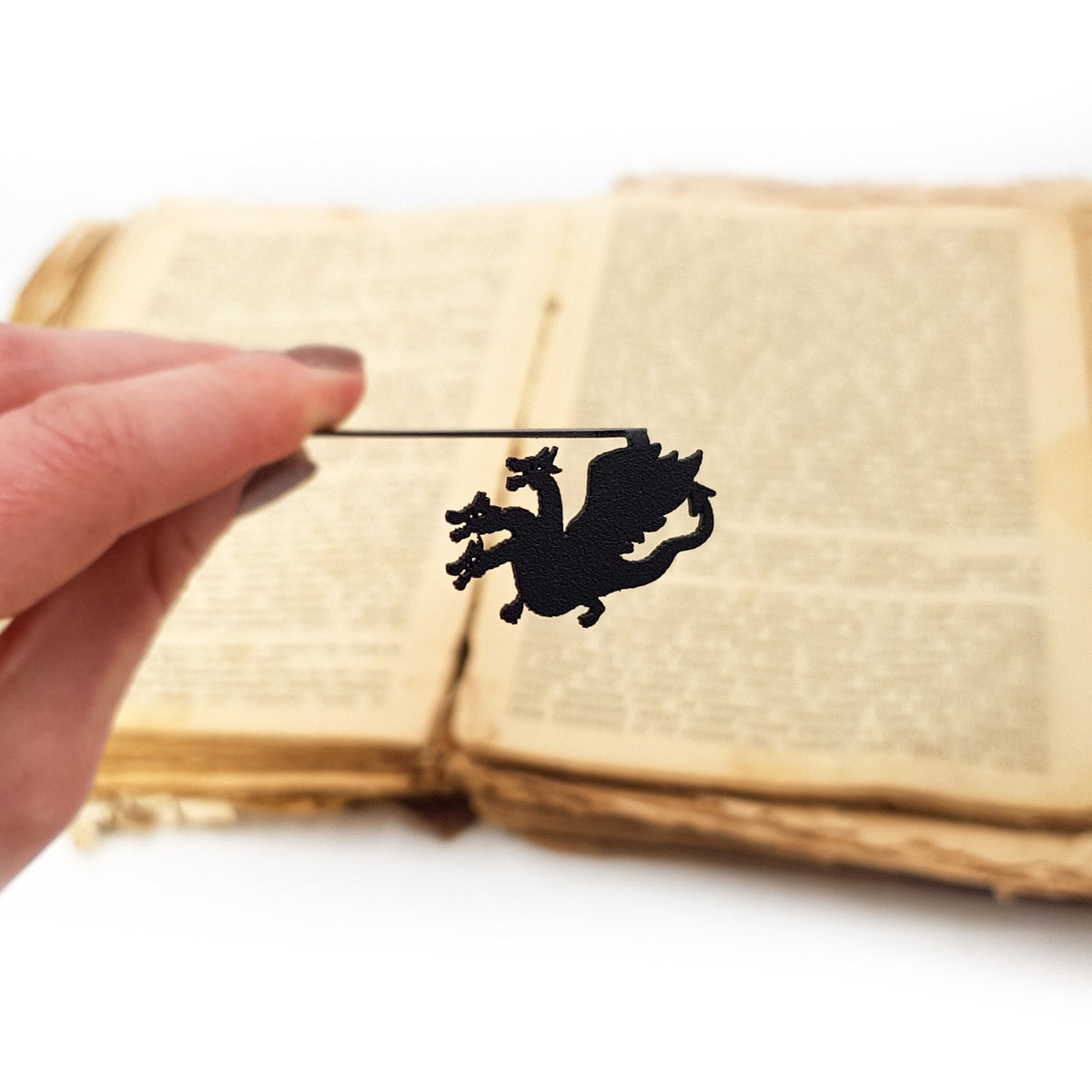 Three Headed Dragon metal bookmark held in a hand above an open book