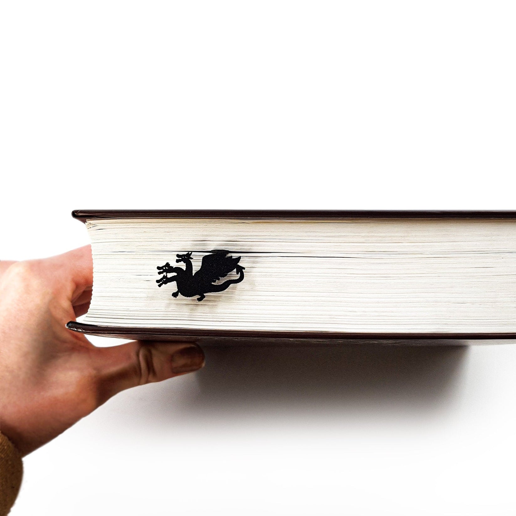 Three Headed Dragon metal bookmark held up beside an open book