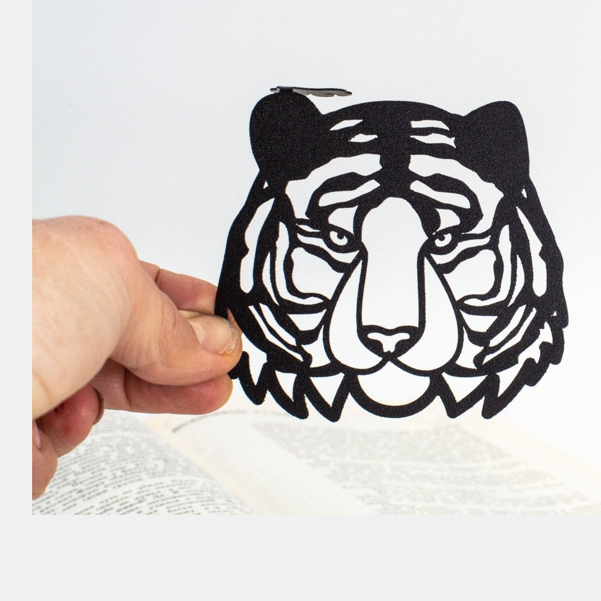 Tiger Head metal bookmark held in a hand above an open book