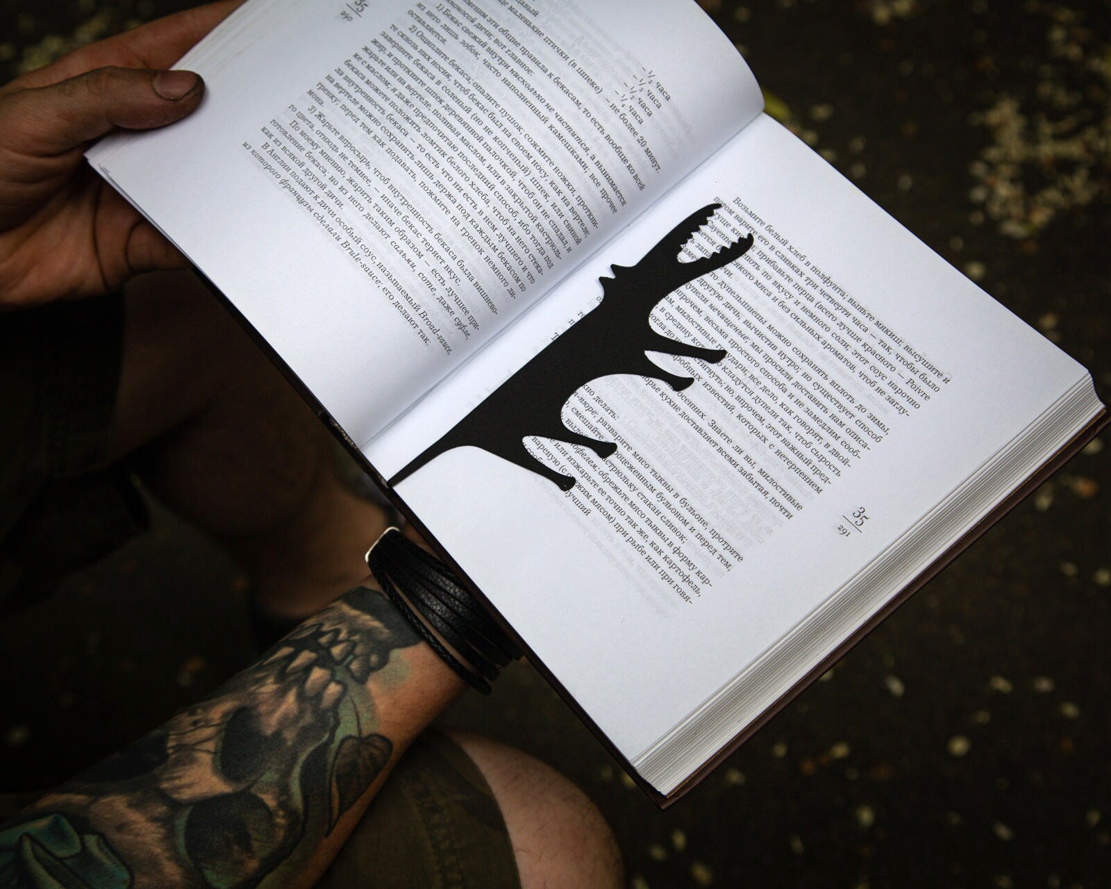 Hungry Wolf metal bookmark held in a hand above an open book