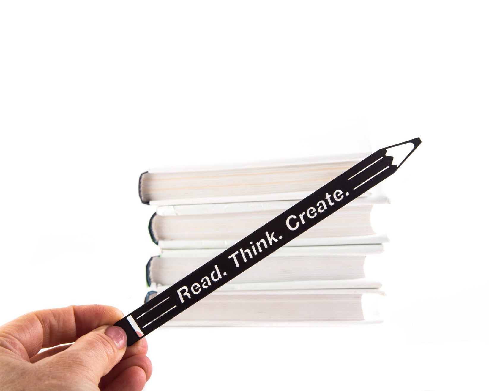 Pencil Read, Think, Create metal bookmark held in a hand above an open book