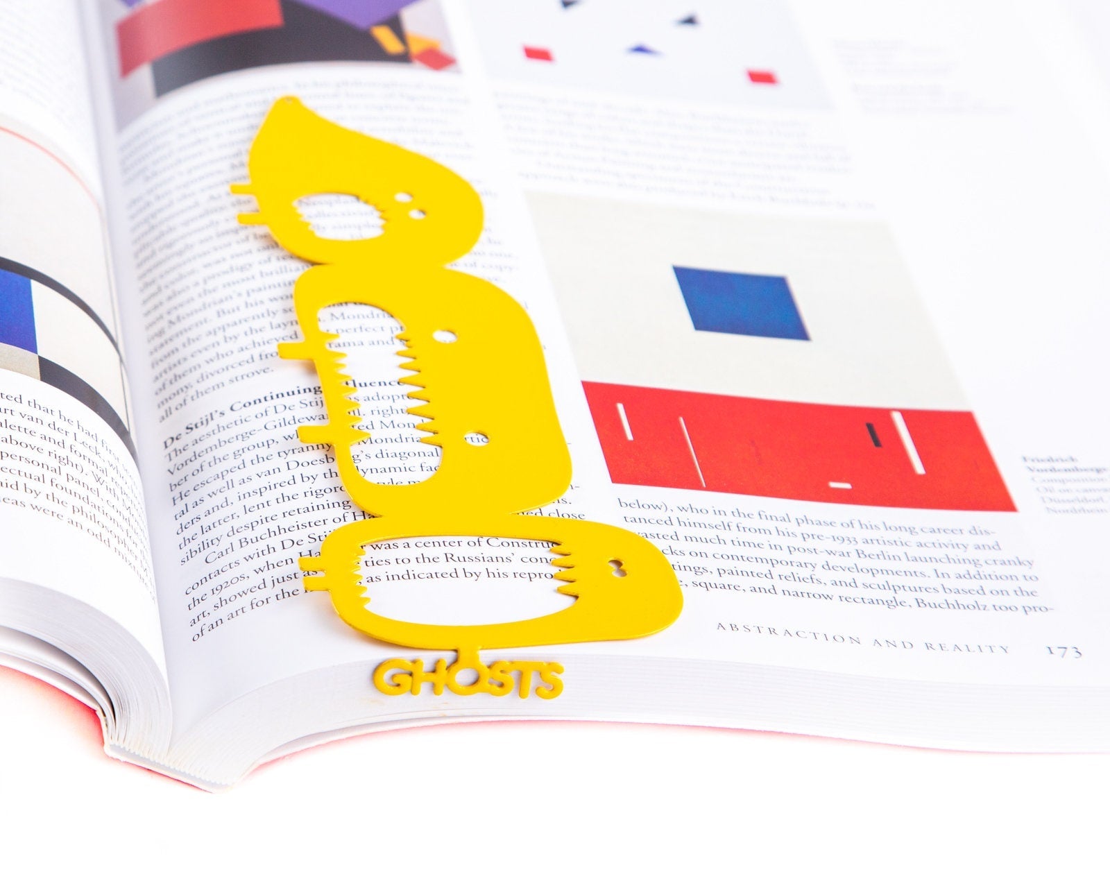 Three Screaming Monsters metal bookmark in gold resting on the pages of an open book