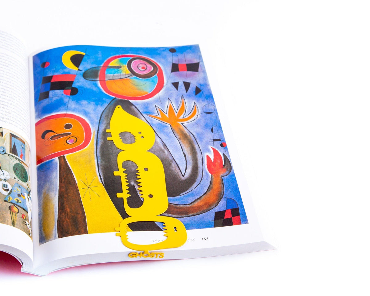 Three Screaming Monsters metal bookmark in gold placed on a colour illustration