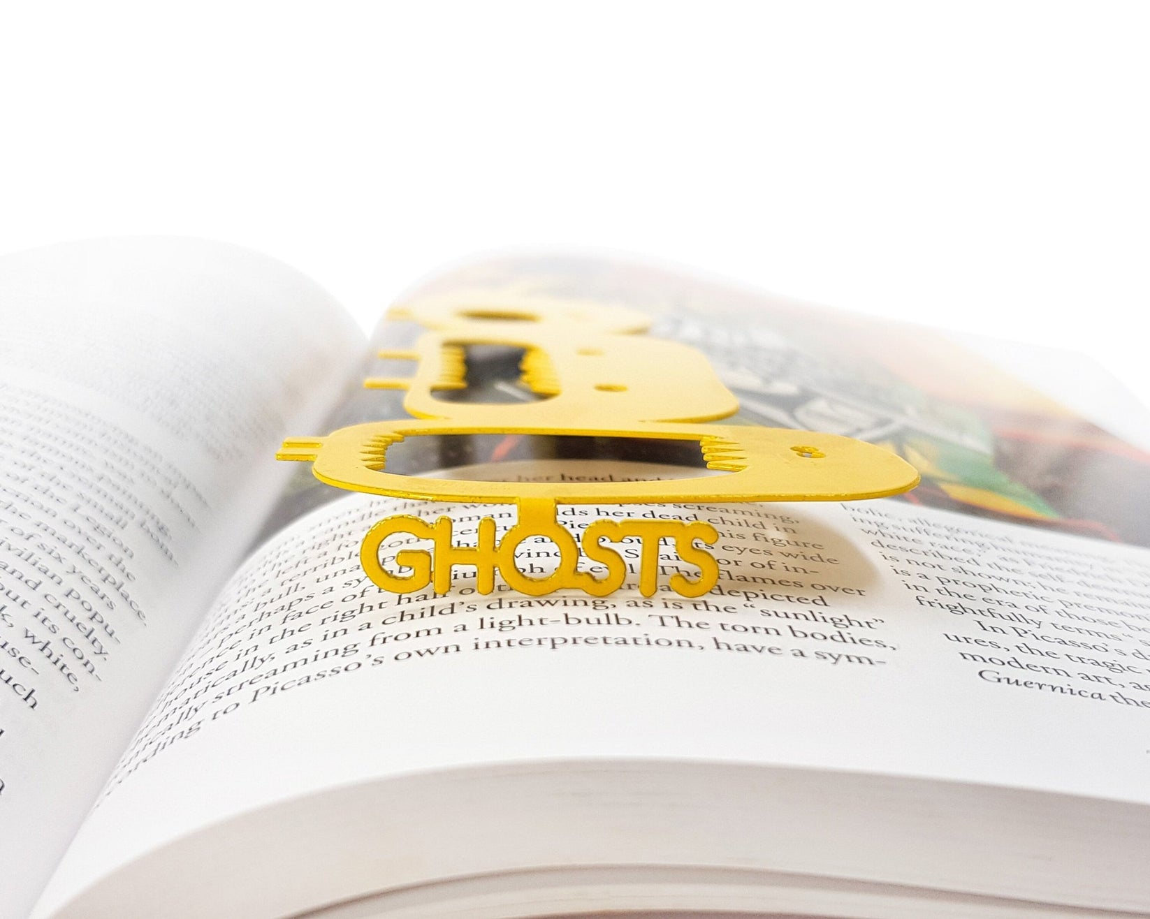 Three Screaming Monsters metal bookmark in gold marking a page in an illustrated book, view 4