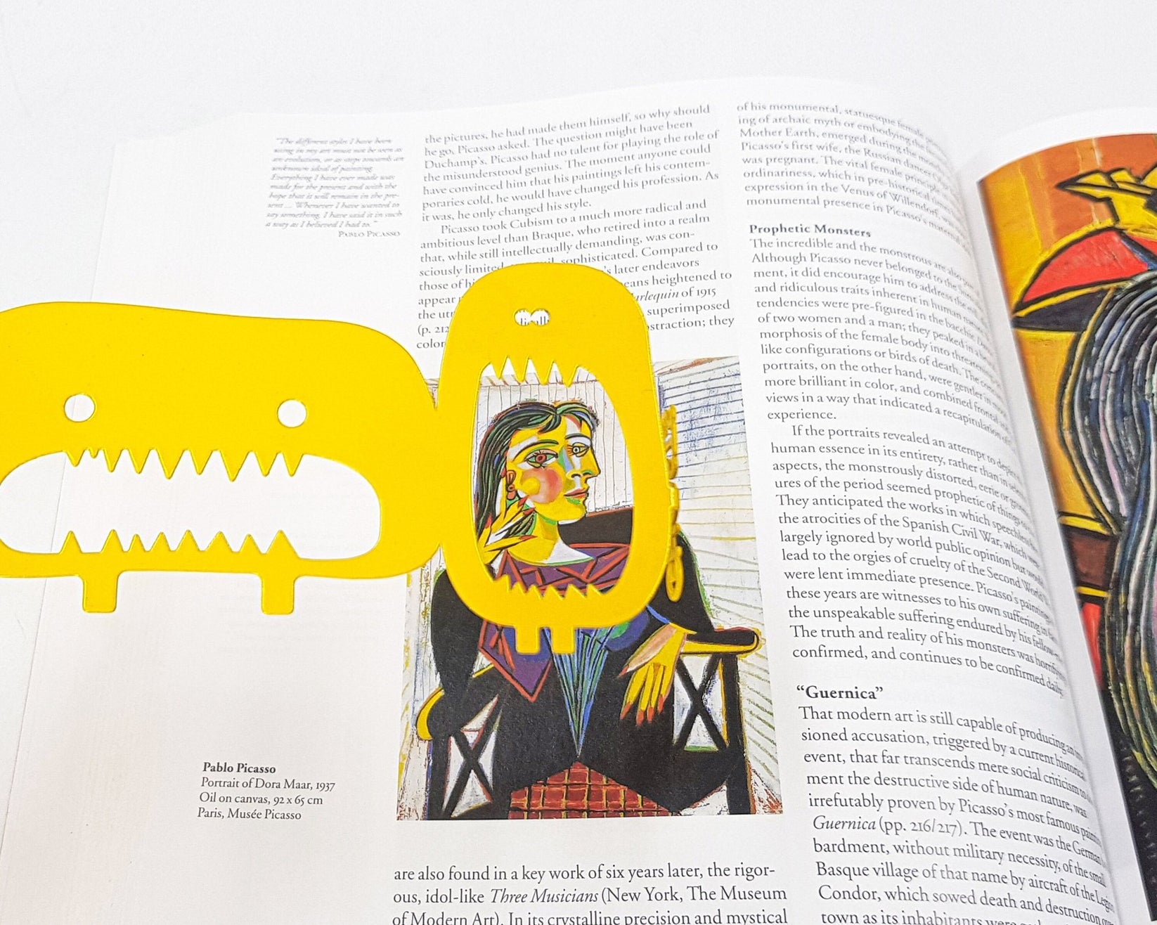 Three Screaming Monsters metal bookmark in gold marking a page in an illustrated book