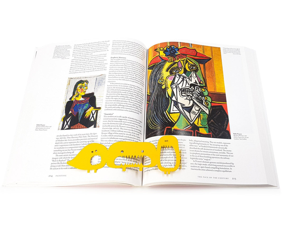 Three Screaming Monsters metal bookmark in gold on an illustrated page, view 5