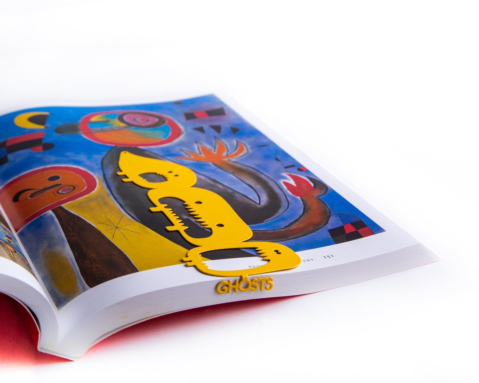 Three Screaming Monsters metal bookmark in gold on an illustrated page