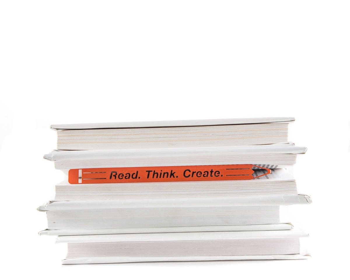 Read. Think. Create. Pencil metal bookmark in red lying on a stack of white books