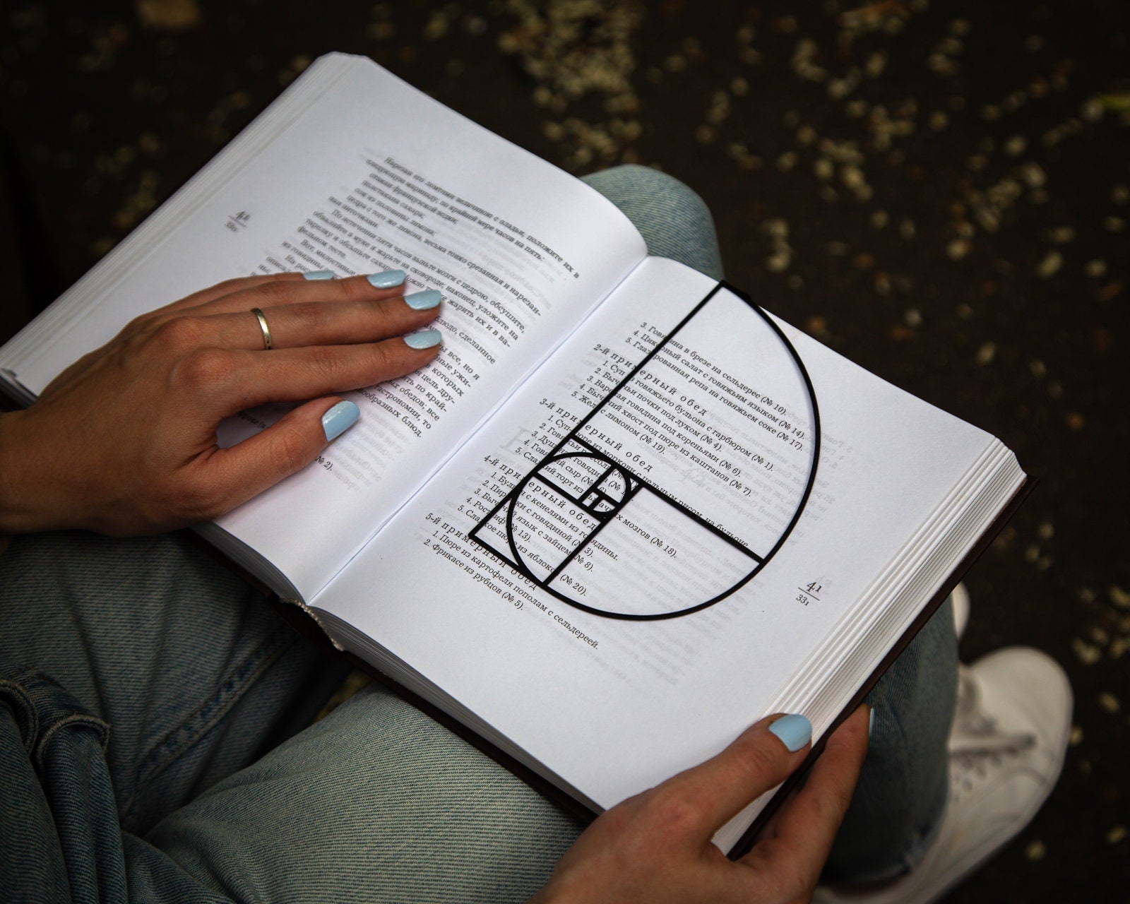 Golden Ratio metal bookmark held in a hand above an open book