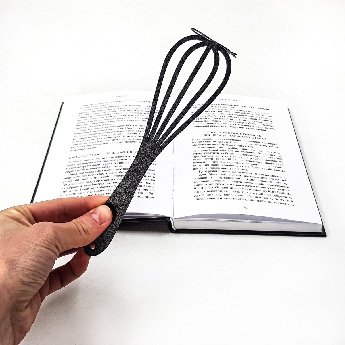 Whisk metal bookmark held up beside an open book