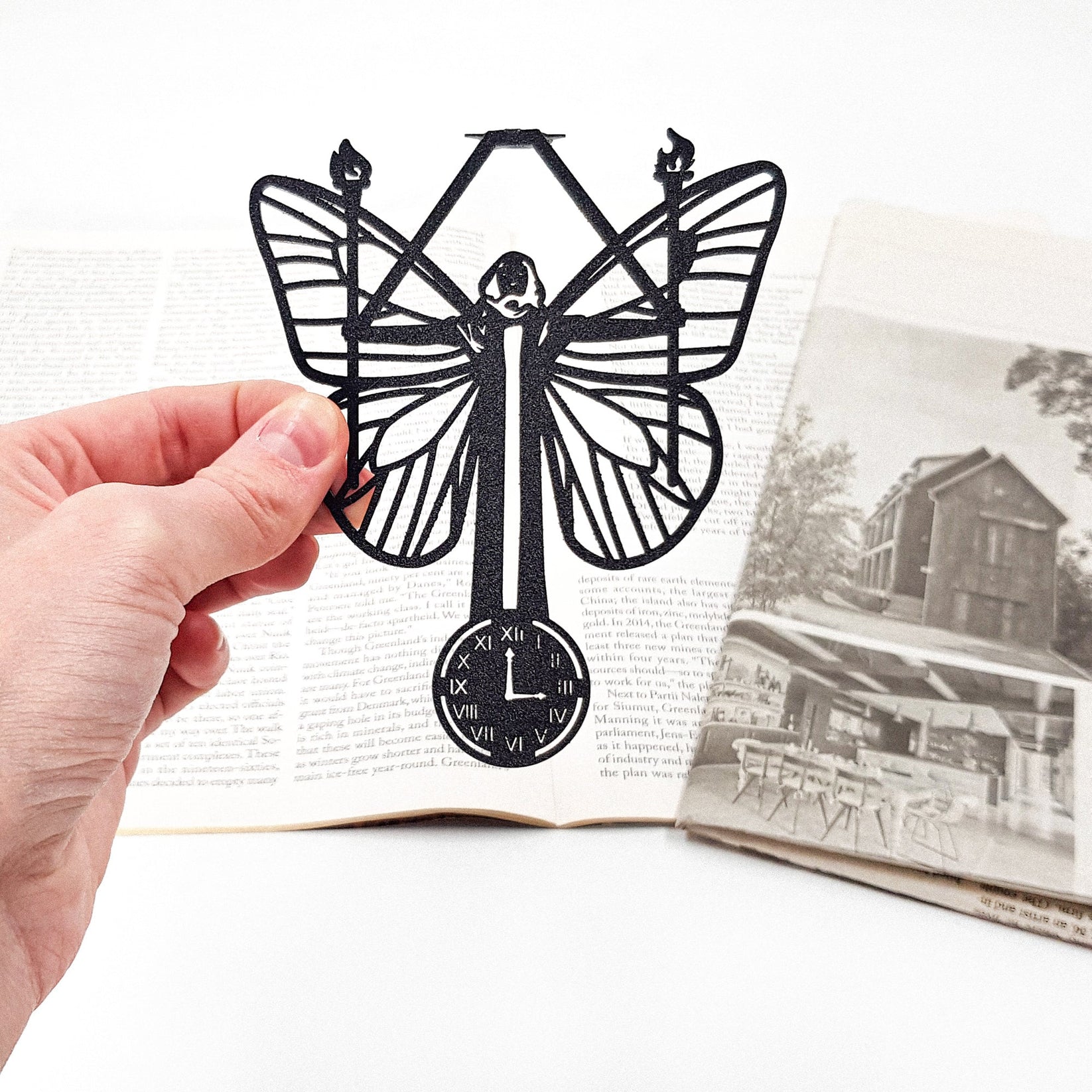 Witch Hour metal bookmark held in a hand above an open book