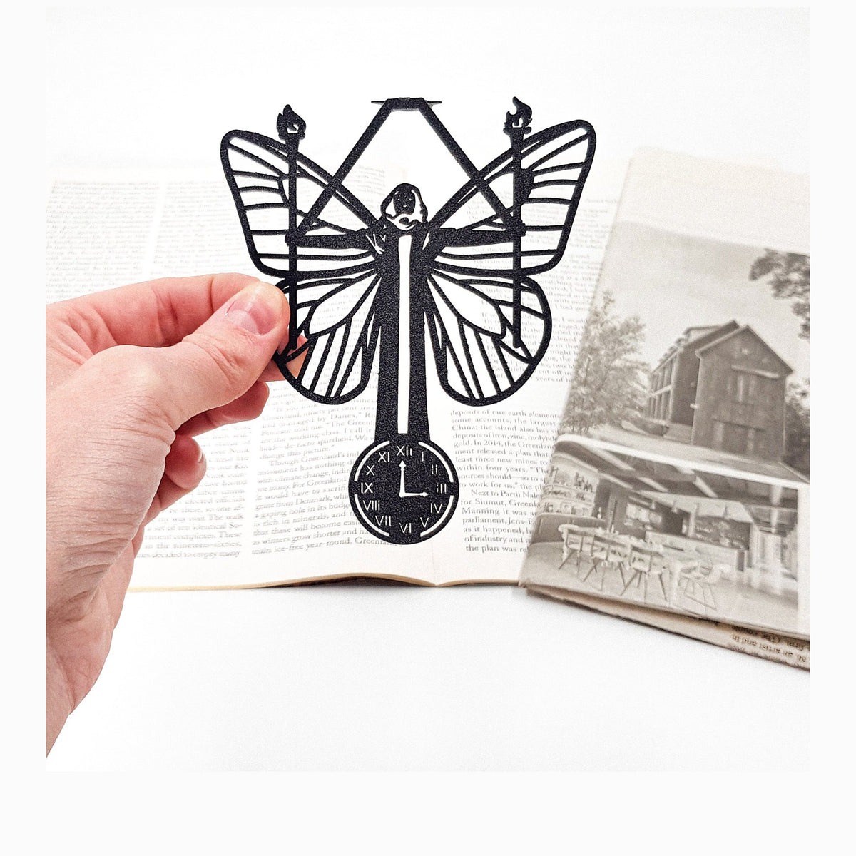 Witch Hour metal bookmark held in a hand above an open book