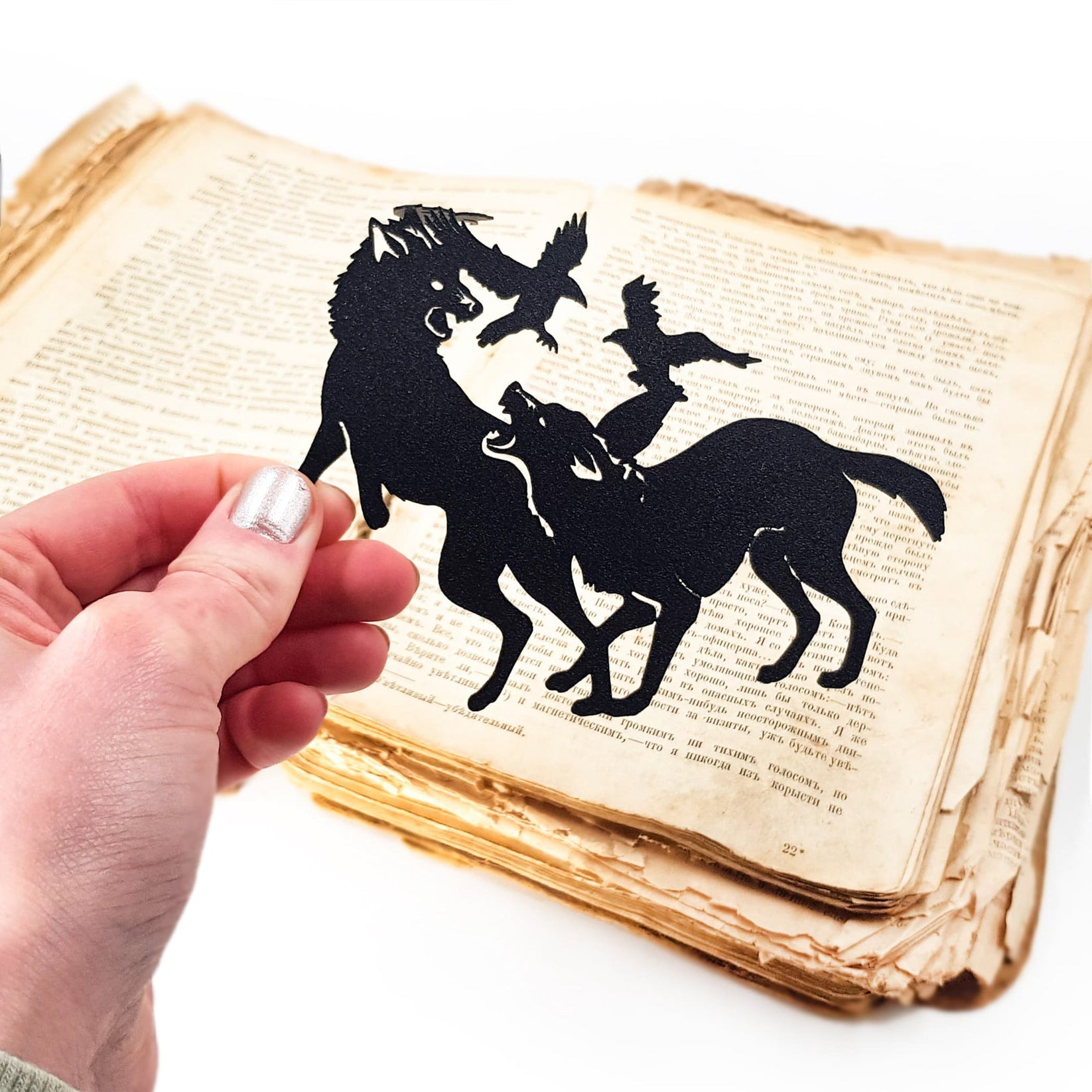 Wolves & Raven metal bookmark held up beside an open book