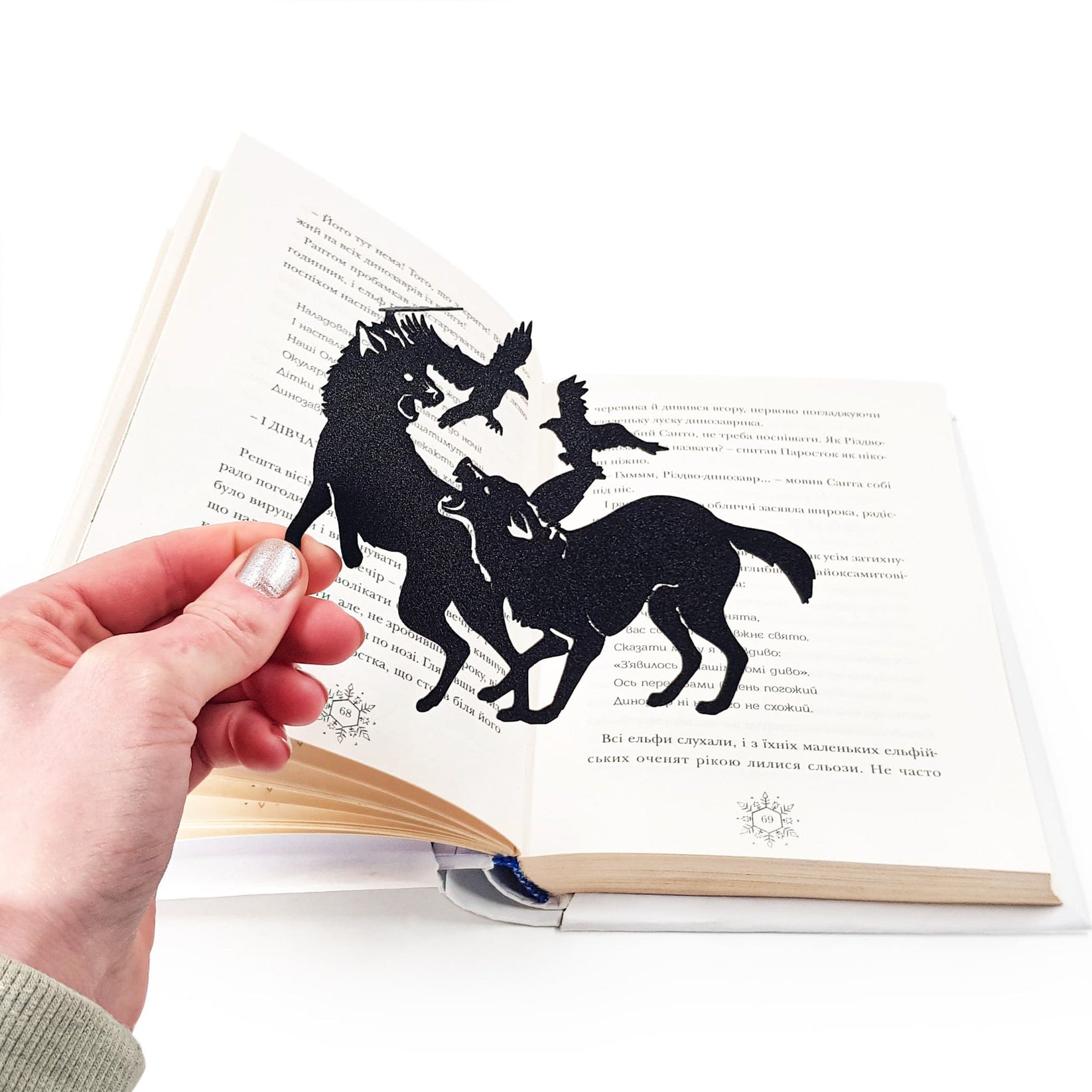 Wolves & Raven metal bookmark held in a hand above an open book