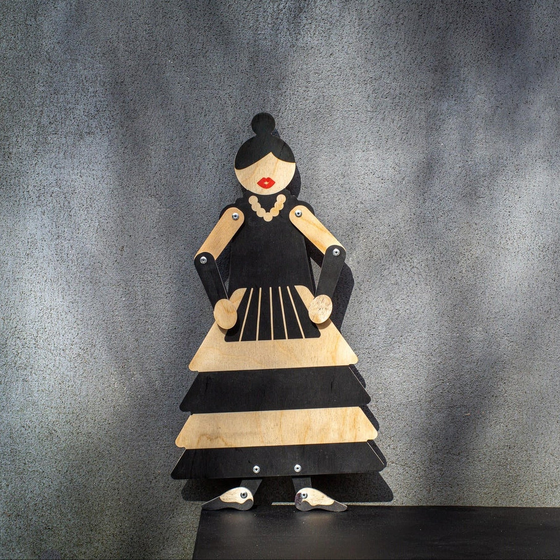 Wooden flamenco puppet displayed on black shelf against grey wall, arms posed at sides