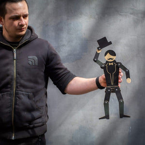 Maker holding wooden gentleman puppet at arm's length showing scale — tuxedo figure tipping top hat