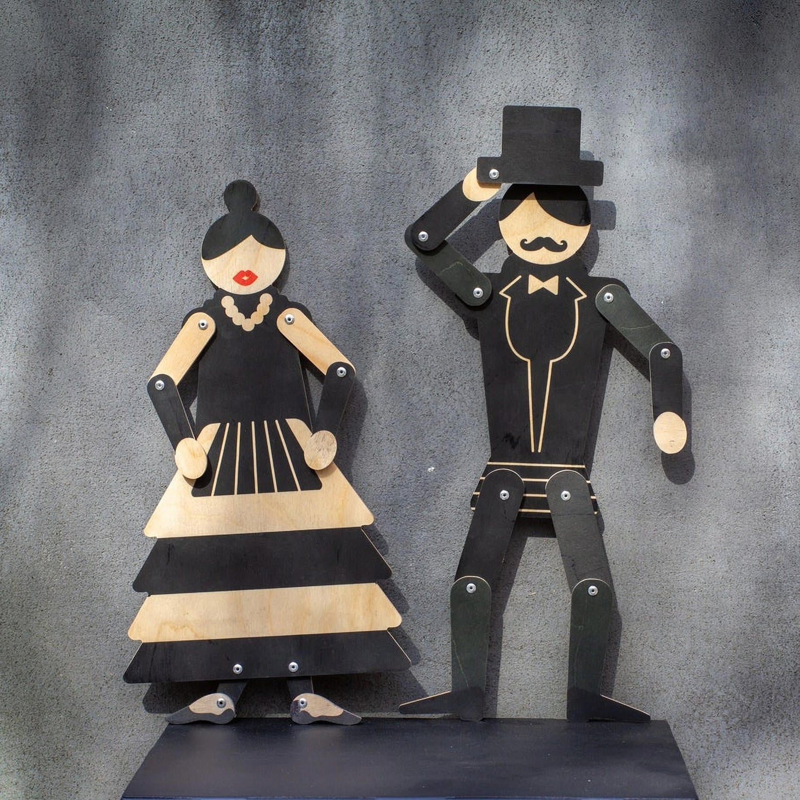 Wooden gentleman and flamenco dancer puppets displayed as a pair on dark shelf against grey wall