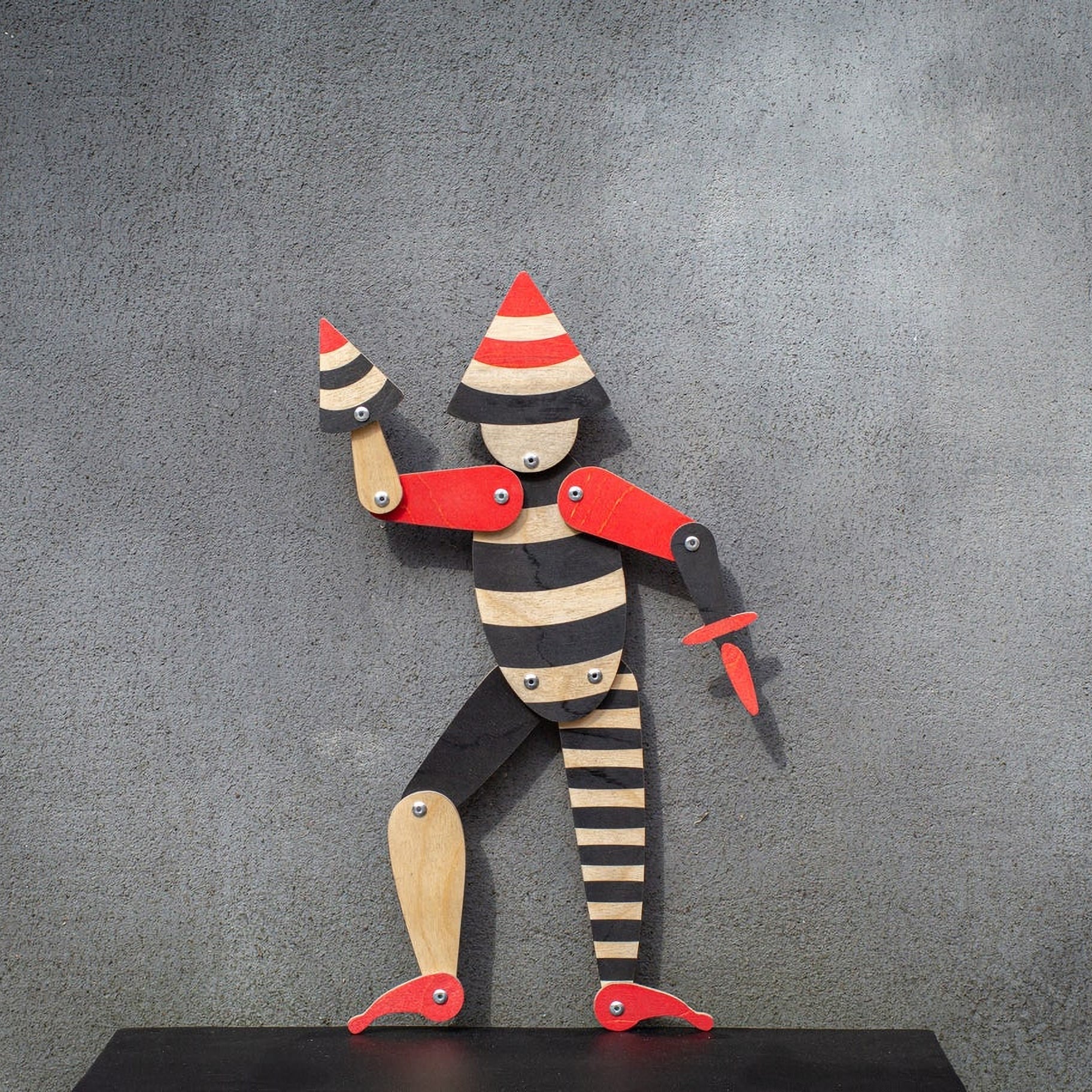 Handmade articulated plywood acrobat puppet standing against wall, full body view