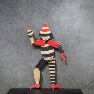 Handmade articulated plywood acrobat puppet standing against wall, full body view