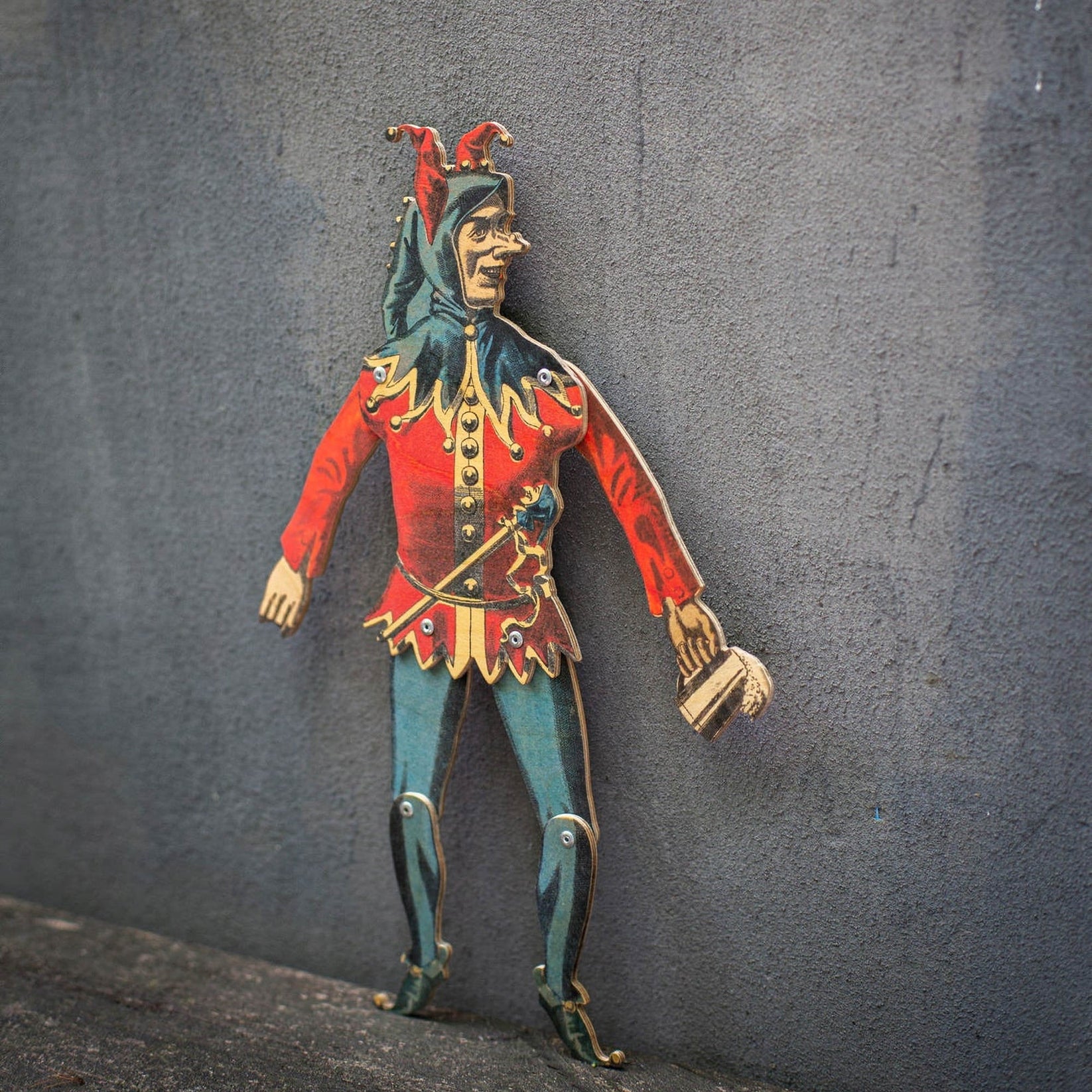 plywood jester puppet articulated movable joints standing against textured wall