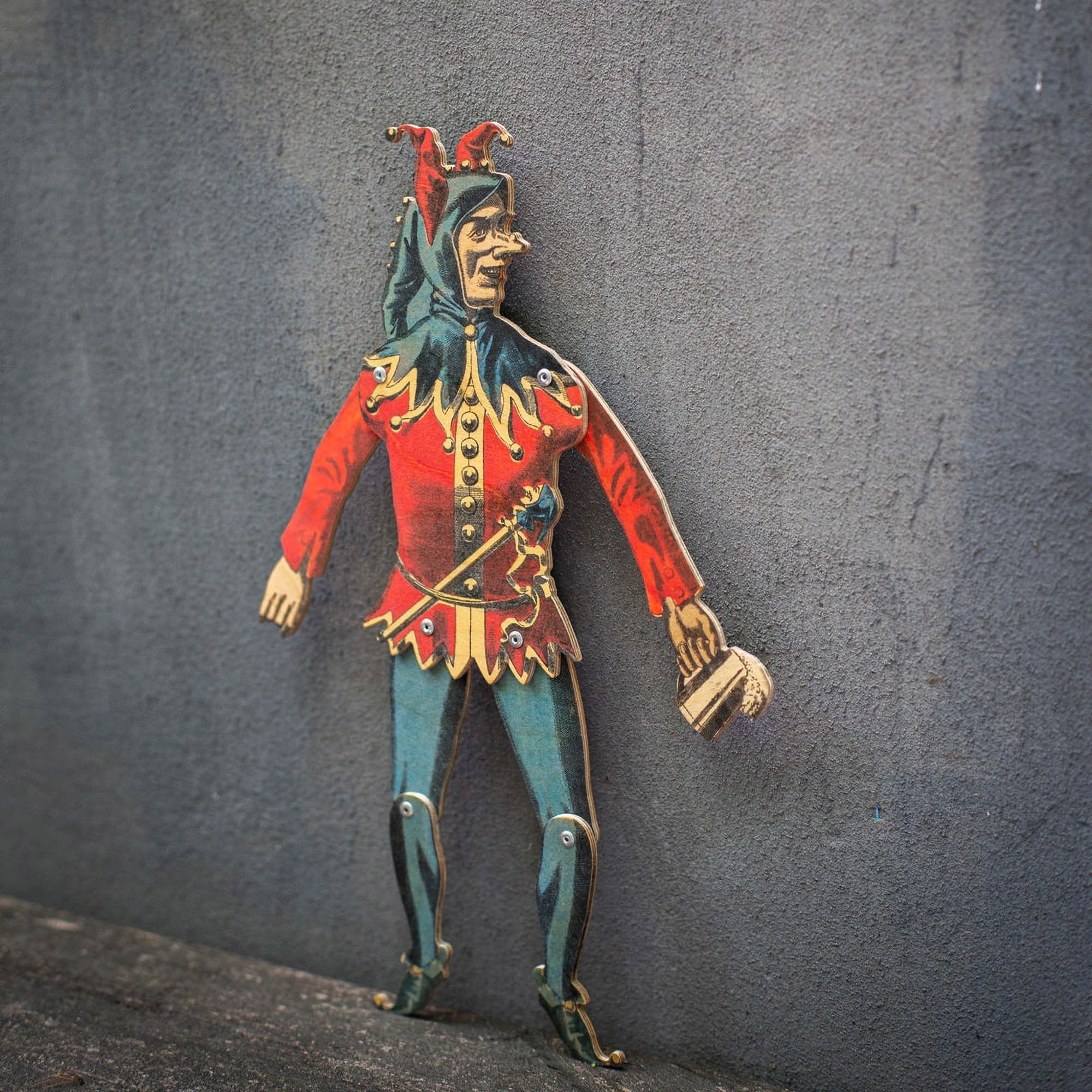 plywood jester puppet articulated movable joints standing against textured wall