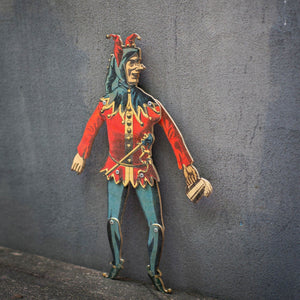 plywood jester puppet articulated movable joints standing against textured wall